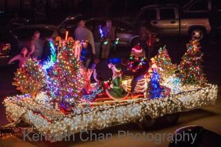Photo of children dressed as elves, smoky the bear, and Christmas trees on a float covered in colorful Christmas lights